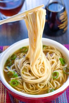 someone is holding chopsticks over a bowl of noodles with soup in the background