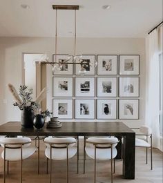 a dining room table with white chairs and pictures on the wall behind it, all in black and white