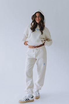 a woman in white sweatsuit and hat standing with her hands on her hips