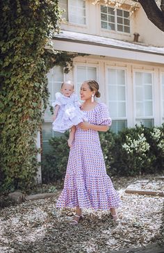 a woman holding a baby in front of a house