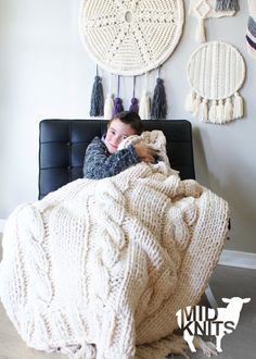 a woman laying in bed under a blanket with tassels hanging on the wall