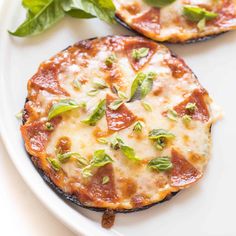 two small pizzas on a white plate with basil and pepperoni leaves around them