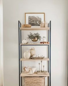 a shelf with baskets and vases on it in the corner of a living room