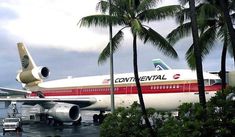 an airplane sitting on the tarmac with palm trees around it