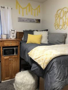 a bedroom with gray and yellow bedding, white rugs and a microwave in the corner