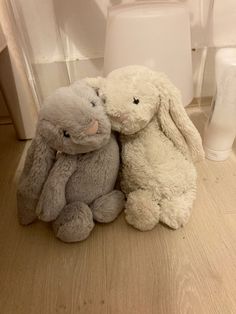 two stuffed animals sitting next to each other on the floor in front of a toilet