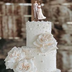 a wedding cake decorated with white flowers and a bride and groom figurine on top