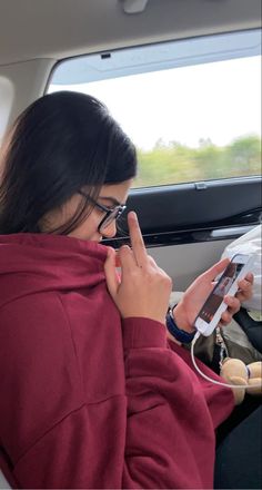 a woman sitting in the back seat of a car using her cell phone and listening to headphones