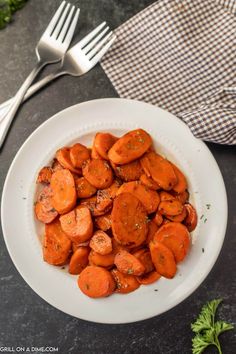 a white bowl filled with cooked carrots next to a fork and napkin on top of a table