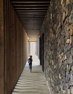 a person walking down a long hallway between two walls covered in wood planks and stone