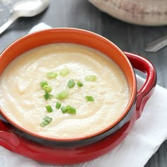 a red bowl filled with soup sitting on top of a white napkin next to a spoon