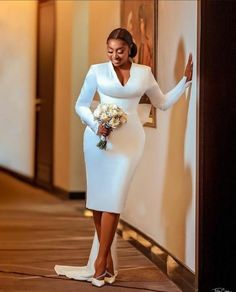 a woman in a white dress leaning against a wall