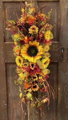 a sunflower wreath hanging on a door with autumn leaves and flowers in the center