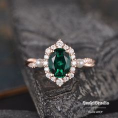 an oval shaped green and white diamond ring on top of a black rock with pearls around the band