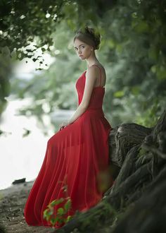 a woman in a red dress sitting on a tree branch