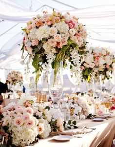 a table topped with lots of flowers next to tall vases filled with white and pink flowers