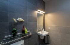 a bathroom with gray tile walls and flooring, including a white sink and mirror