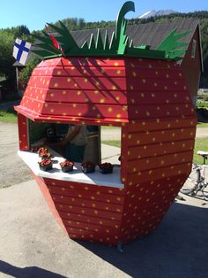 a large strawberry shaped building with people standing around it in front of the fruit stand