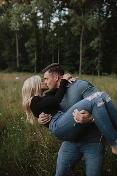 a man and woman kissing in the middle of a field with trees in the background