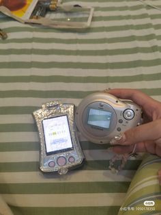 a person holding an electronic device on top of a striped table cloth with other items in the background