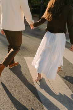 a man and woman walking across a cross walk holding each other's hands as they hold hands