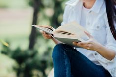 a woman sitting down reading a book in her lap and looking at the pages with both hands