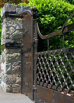 an iron gate is open to reveal a stone wall and shrubbery in the background