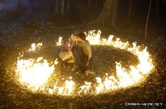 a man and woman sitting in the middle of a fire pit with their arms around each other