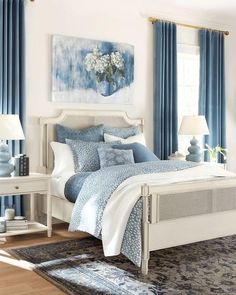 a bedroom with blue and white bedding, curtains and rugs on the floor