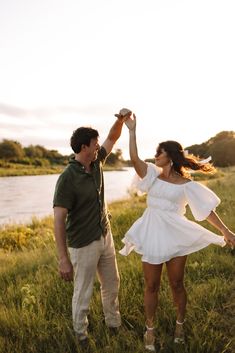 a man and woman holding hands while standing in the grass near a body of water