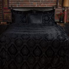 a bed with black bedspread and pillows in front of a brick wall