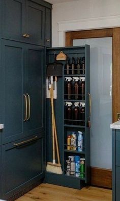 an open cabinet in the middle of a kitchen with brooms and cleaning supplies inside