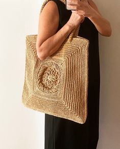 a woman holding a cell phone while standing next to a wall with a straw bag on it