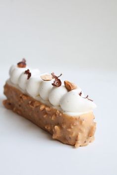 a piece of cake with nuts and whipped cream on top, sitting on a white surface