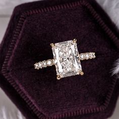 an engagement ring with a princess cut diamond surrounded by small round diamonds in a velvet box