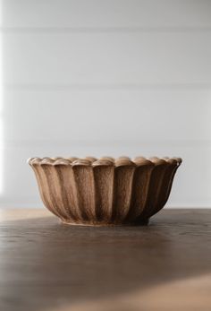 a wooden bowl sitting on top of a table next to a white wall and floor