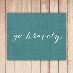 the word go bravely written in white ink on a teal green background with wood planks