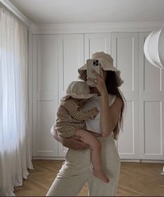 a woman taking a selfie while holding a baby in her arms and wearing a hat