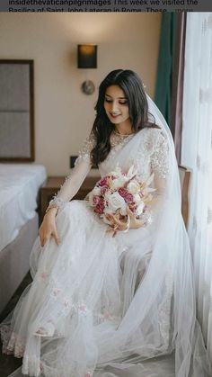 a woman in a white wedding dress sitting on a bed holding a bouquet of flowers