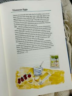 an open book with illustrations on the page and in front of it is a bowl of strawberries