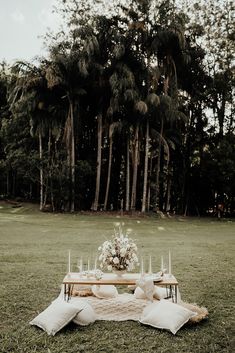 a table with candles and flowers on it in the middle of a field near some trees