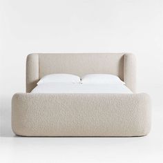 an upholstered bed with white sheets and pillows