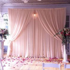 a wedding ceremony setup with pink flowers on the floor and drapes draped over it