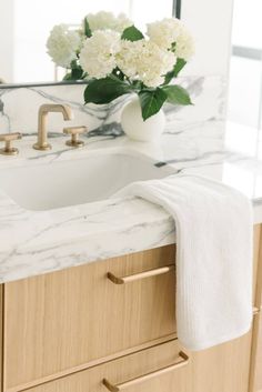 a bathroom sink with marble counter top next to a mirror and flowers in a vase