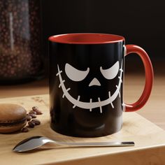 a black and red coffee mug sitting on top of a wooden table next to a spoon