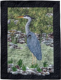 a quilted picture of a bird standing in the grass with rocks and water behind it