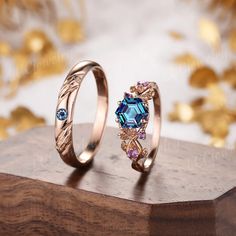 two gold rings with blue and pink stones on top of a wooden stand next to each other