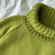 a green sweater laying on top of a white sheet