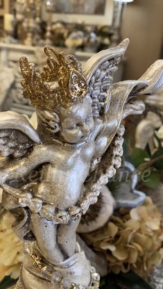 a statue of an angel with gold wings and pearls on it's body, surrounded by flowers