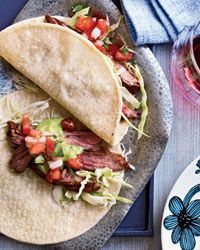 two tacos are sitting on a plate next to a glass of wine and a blue napkin